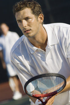 Close-up of mid adult man holding racket with partner in the background