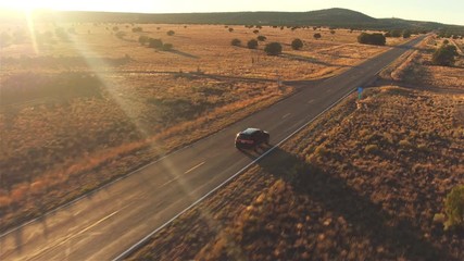 AERIAL: Black car driving along empty country road at golden summer sunset - Powered by Adobe