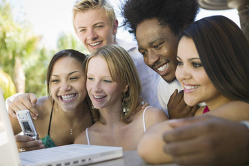 Group of friends at back yard table using laptop and cell phone close up