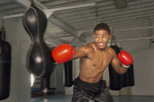 African American Male Boxer Hitting Punch Bag In Red Gloves In The Gym