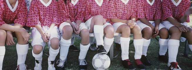Low section of female soccer players sitting side by side - Powered by Adobe