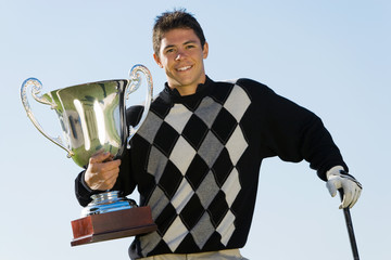 Portrait of a happy young male golfer holding trophy against clear sky