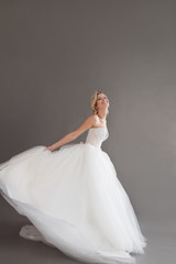 Fototapeta premium Dancing young bride in luxurious wedding dress. Pretty girl in white. Emotions of happiness, laughter and smile, gray background