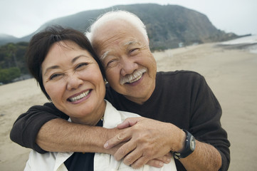 Closeup portrait of a happy senior man embracing woman from behind on the beach