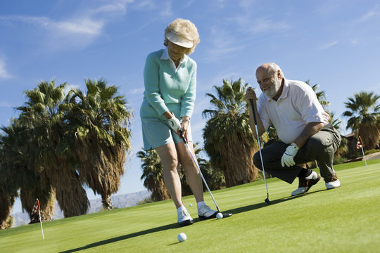 Happy Senior Female With Male Friend Playing Golf