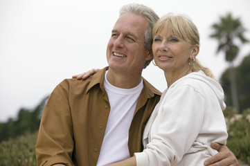Fototapeta premium Thoughtful middle aged couple looking away while embracing each other on beach