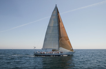 Side view of a group of crew members sitting on the side of a sailboat in the ocean against sky