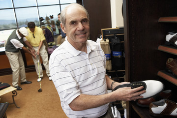 Portrait of happy senior man selecting shoes in store with people in background