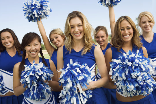 Group portrait of young cheerleaders holding pom-poms on field