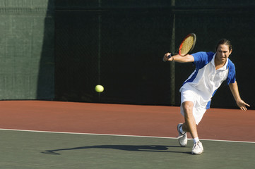 Full length of a male tennis player hitting backhand on the tennis court