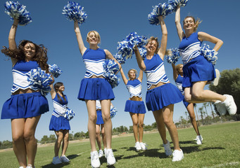 Excited young cheerleaders with pompoms cheering on field