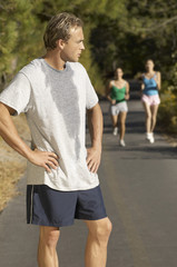 Male jogger pausing for breath on path with female friends in background