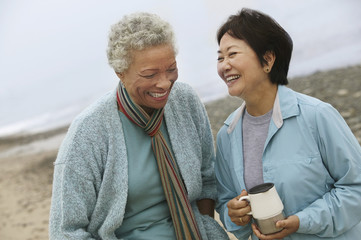 Fototapeta premium Dwie wesołe przyjaciółki w średnim wieku rozmawiają na plaży