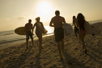 Group of friends with surfboards running towards ocean at sunset