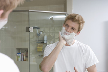 Man applying shaving cream on face in front of mirror