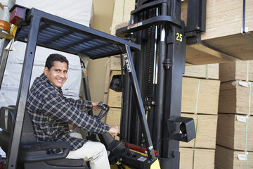 Portrait of happy mature warehouse worker stacking wood by forklift