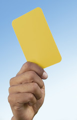 Close-up of referee's hand holding a yellow card that indicates a warning to a player for a foul
