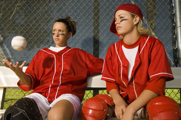 Two confident softball players sitting on the bench in dugout - Powered by Adobe