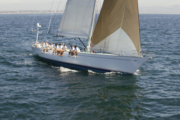 Obraz premium Group of crew members sitting on the side of a sailboat in the ocean