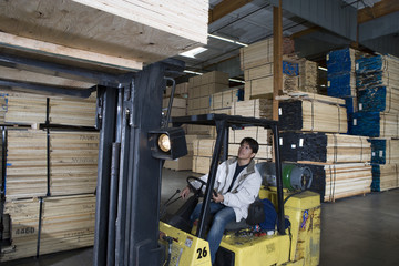 Mid adult worker stacking wood by forklift at warehouse