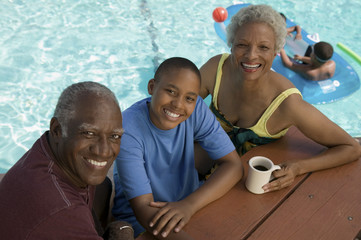 Boy (13-15) sitting with grandparents at picnic table by swimming pool elevated view portrait.