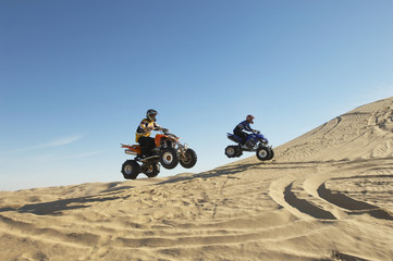 Side view of two men doing wheelies on quad bikes in the desert