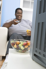 Fototapeta premium Happy African obese man watching television while holding glass of juice