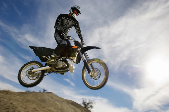 Low angle view of motocross racer in midair against cloudy sky