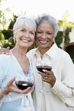 Portrait of happy senior female friends standing outside with wine glasses