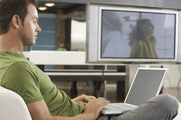 Side view of young man using laptop on sofa in modern apartment