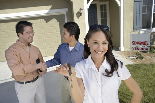 Portrait of young woman holding keys while man shaking hands with agent in background