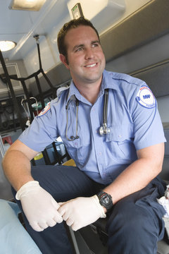 Happy middle aged EMT doctor sitting in ambulance and looking away