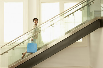 Happy young woman walking up the modern stairs with shopping bag