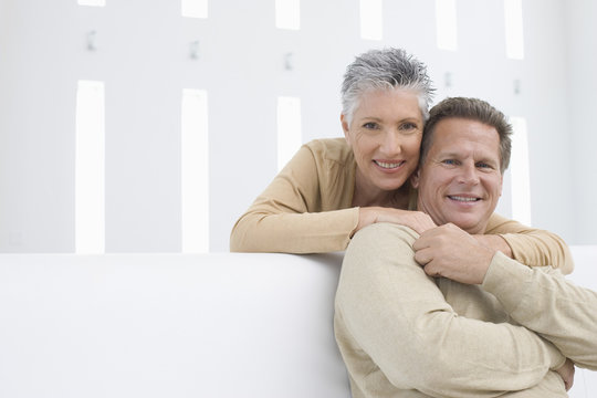 Portrait Of Happy Senior Woman Embracing Man From Behind At Home