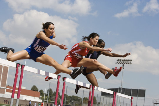 Multiracial female athletes clearing hurdles in race