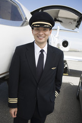 Portrait of happy Japanese pilot standing by airplane at airfield