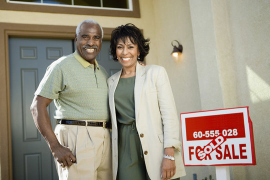 Portrait of smiling African American couple standing by sold real estate sign
