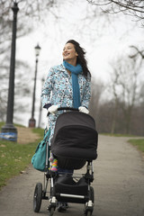 Happy young mother walking with baby carriage in park