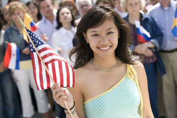 Portrait of young woman holding American flag with people in the background