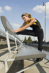 Fit Caucasian woman in sportswear working out at stadium bench