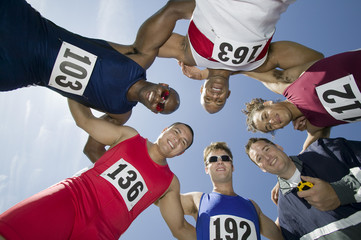Group of multiethnic male athletes with trainer forming a huddle against sky