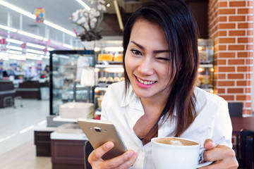 Asian women are bent to look at the phone and drinking coffee, smiling faces. Focus on face.