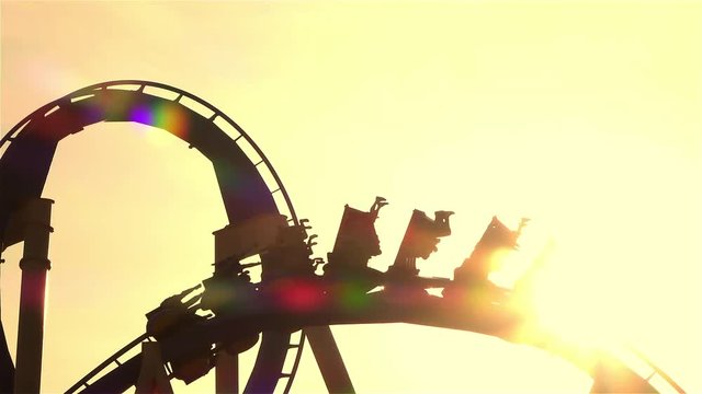 SLOW MOTION CLOSE UP: People riding roller coaster at sunset