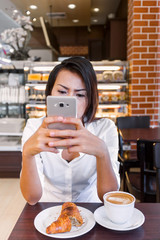 Asia women who drink coffee and look at his cell phone at the same time in a cafe, focus on the face.