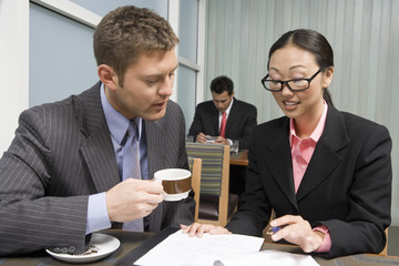 An Asian businesswoman explaining contraction to her business partner with man in the background at restaurant