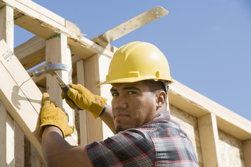 Portrait of a worker hammering a nail to the plank at construction site
