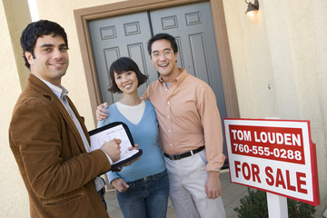 Portrait of happy couple with estate agent standing in front of their new house