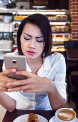 Asia women who drink coffee and look at his cell phone at the same time in a cafe, focus on the face.
