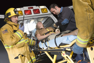 Emergency service people carrying patient on stretcher in ambulance