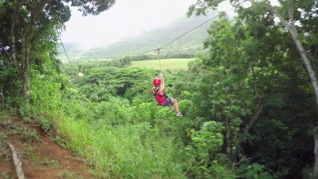 Young smiling girl sliding on cable high above lush jungle rainforest canopies 